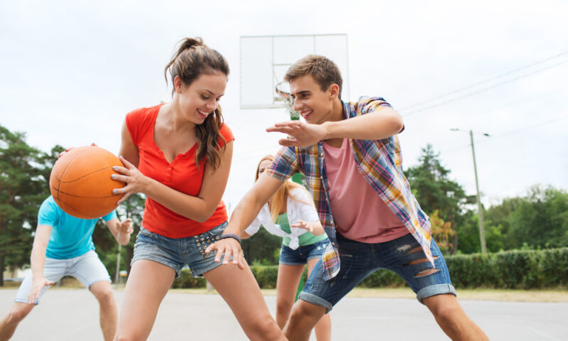 Happy teenagers playing basketball outdoors